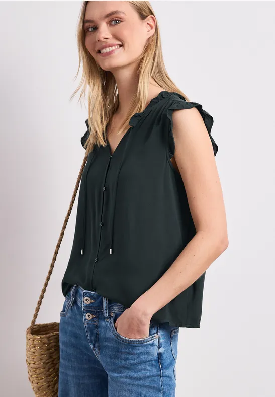 Frau trägt schwarze ärmellose Bluse, Jeans und Strohtasche.