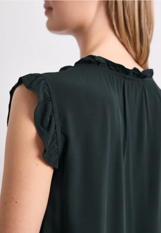 Teilansicht einer Frau von hinten mit schwarzem, ärmellosem Rüschen-Oberteil.