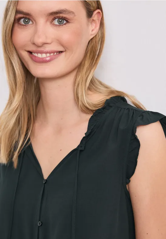 Eine Frau trägt eine ärmellose schwarze Bluse mit Rüschen an den Schultern.