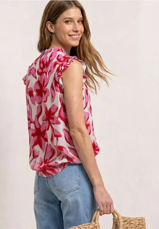 Vrouw in roze bloes met bloemenpatroon en blauwe jeans draagt een gevlochten stroentas opzij.