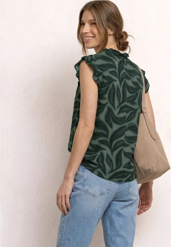 Vrouw van achteren in groen bladpatroon top, lichtblauwe jeans en een beige schoudertas.