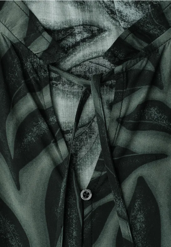 Close-up van een kledingstuk met capuchon, trekkoord en lippenprint in groen-zwart dessin.