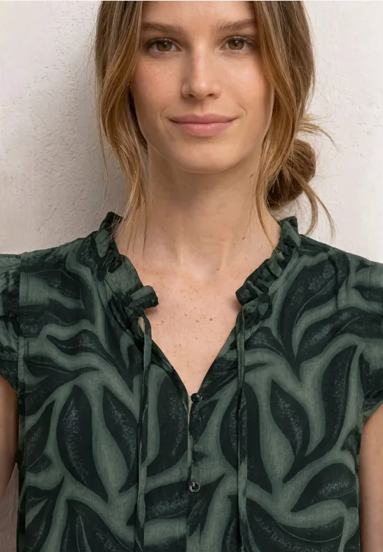 Vrouw in groen, gemusterd topje met V-hals en knoopsluiting, haar losjes in een knot.