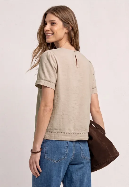 Vrouw van achteren met beige T-shirt met korte mouwen, blauwe jeans en bruine tas voor een lichte achtergrond.