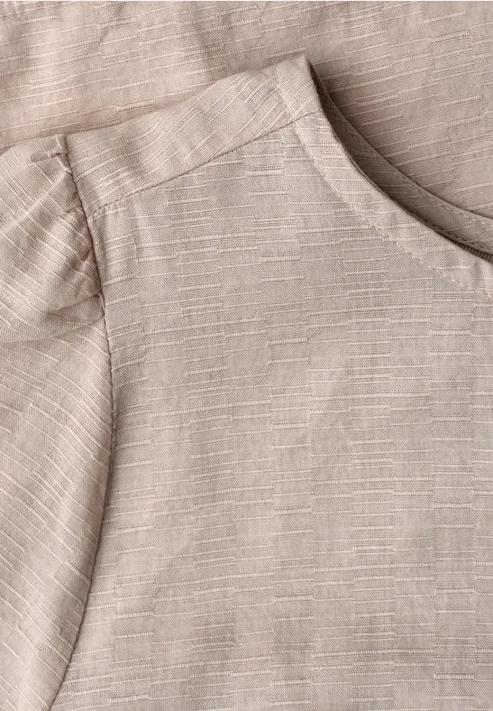 Close-up van een lichtbeige linnen T-shirt met ronde hals en gestructureerde stof.