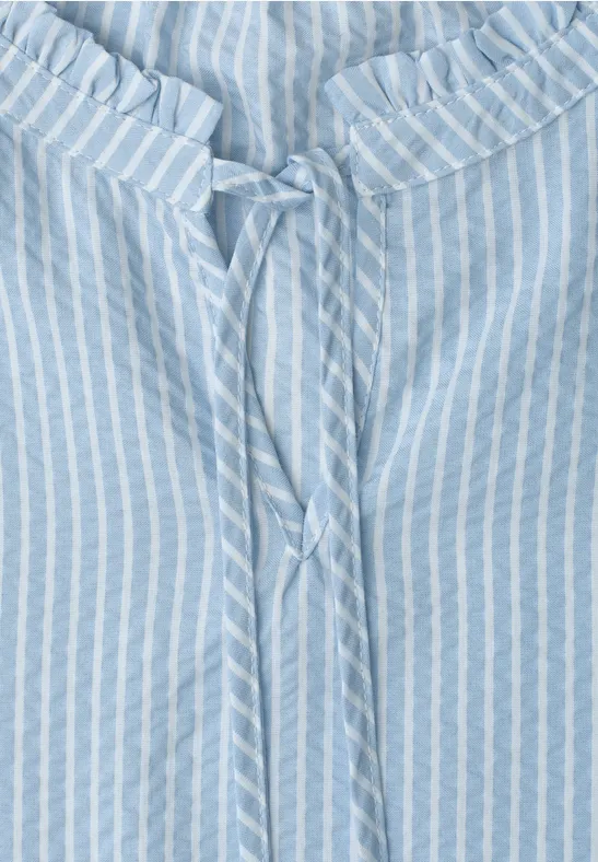 Lichtblauwe blouse met witte strepen en strikje aan de geplooide halslijn.