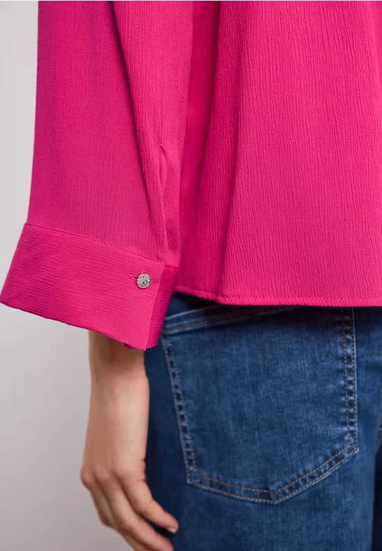 Close-up van een felroze blousemouw met manchet en een hand op een spijkerbroekkzak.