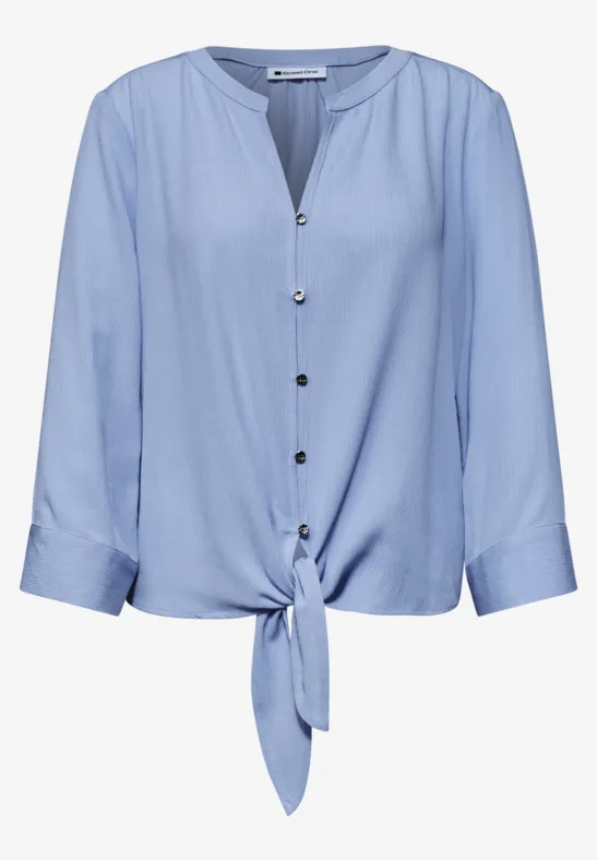 Chemisier bleu clair à boutons, manches 3/4 et lien noué à l'avant.