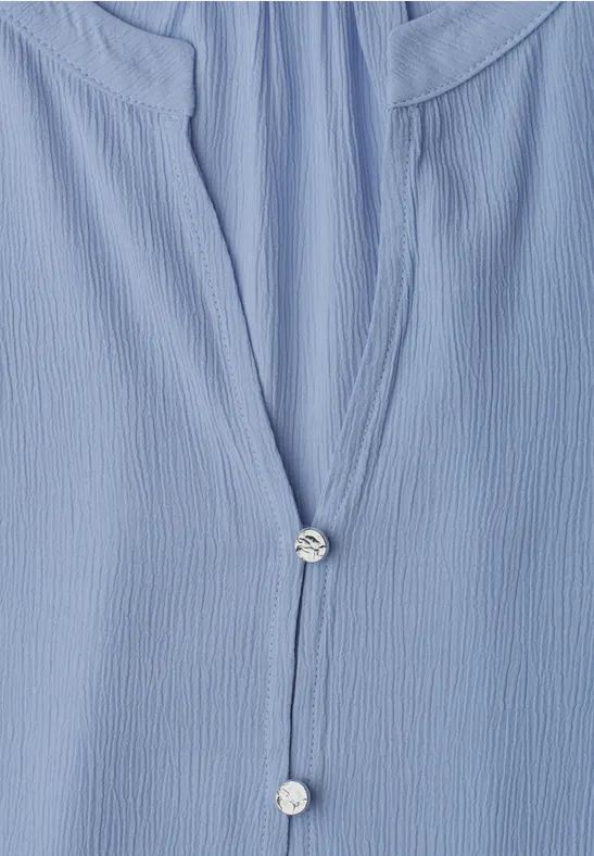 Gros plan sur un chemisier bleu clair gaufré avec petits boutons nacrés.