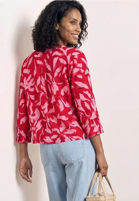 Vrouw van achteren in rood bloemenblouse, blauwe spijkerbroek en rieten tas voor witte achtergrond.