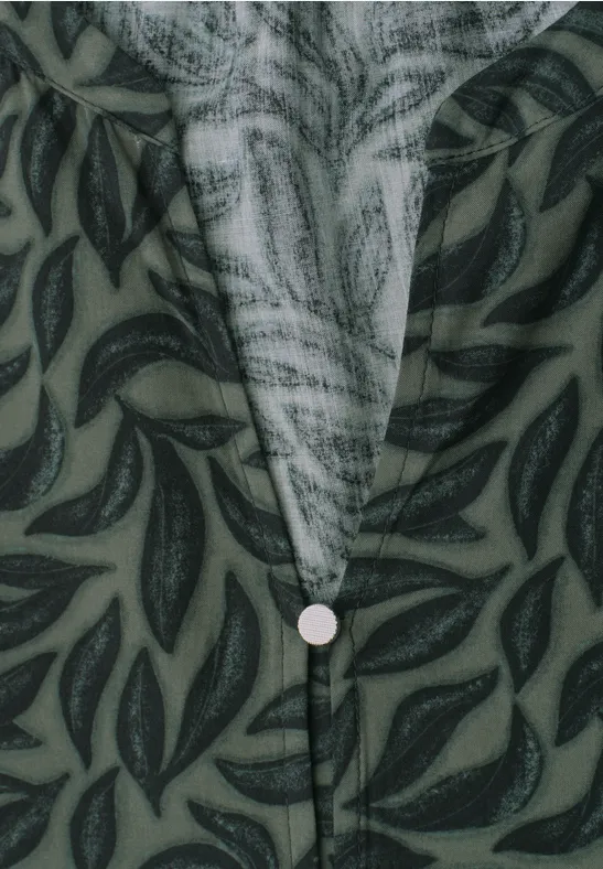Groen overhemd met donker bladpatroon en centrale knoop onder de V-hals (close-up).