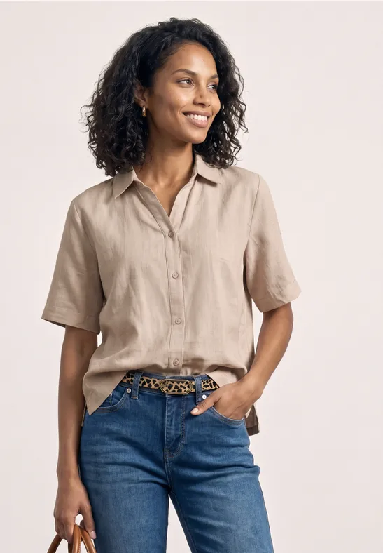 Frau in beiger Kurzarmbluse und blauen Jeans mit Leoprint-Gürtel.