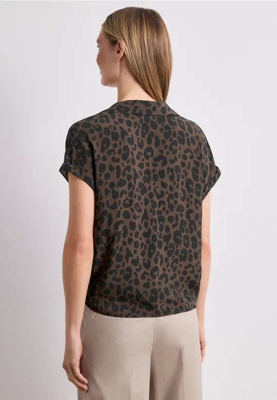 Vrouw van achter in bruin-zwart luipaardprint t-shirt met beige broek, halflang blond haar.
