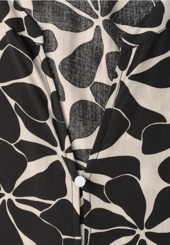 Witte blouse met zwarte, abstracte bloem- en bladpatronen en een zichtbare knoop.
