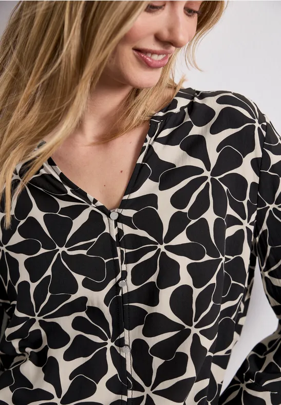Vrouw draagt witte blouse met zwart bloemenprint en V-hals.