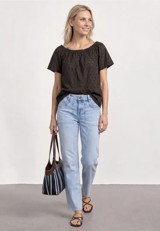 Frau in schwarzem T-Shirt, hellblauen Jeans und Sandalen mit gestreifter Tasche.