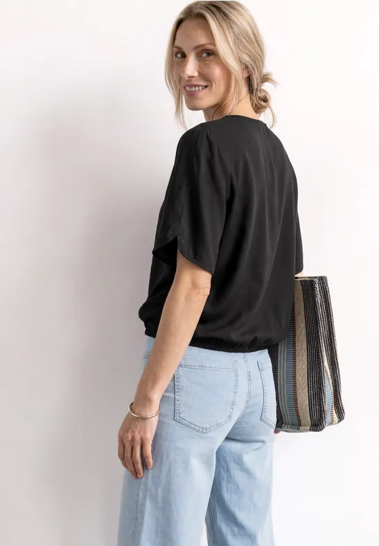 Person von hinten in schwarzem T-Shirt, hellblauen Jeans und großer Umhängetasche.