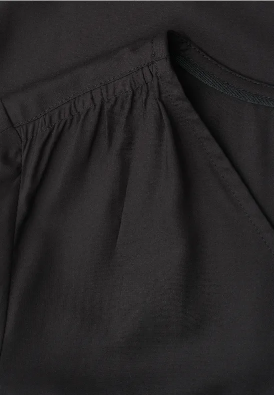 Detailaufnahme eines schwarzen Oberteils mit Falten und Eingrifftasche am Vorderteil.