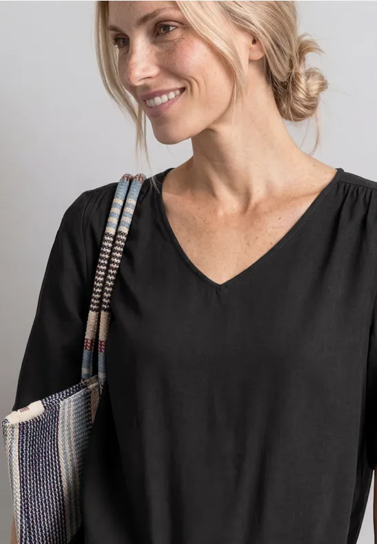 Frau trägt schwarzes V-Shirt und lächelt, hält bunten Schulterbeutel.