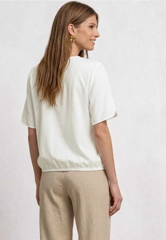 Frau von hinten in weißem T-Shirt und beigen Hosen, helle Wand im Hintergrund.