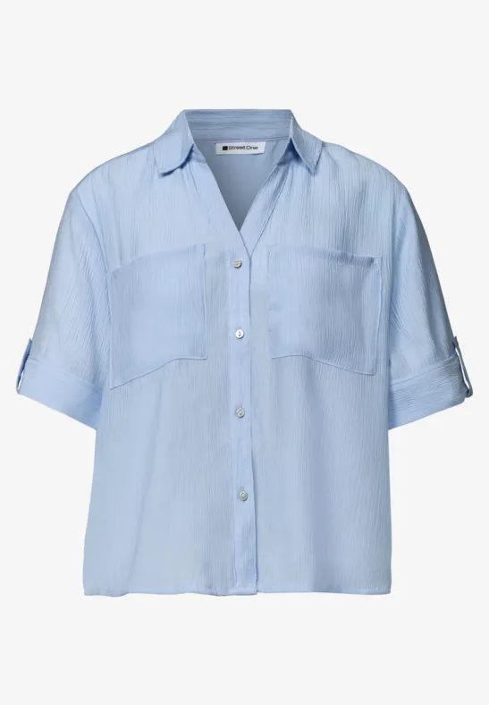 Lichtblauw damesblouse met korte mouwen, borstzakken en knoopsluiting.