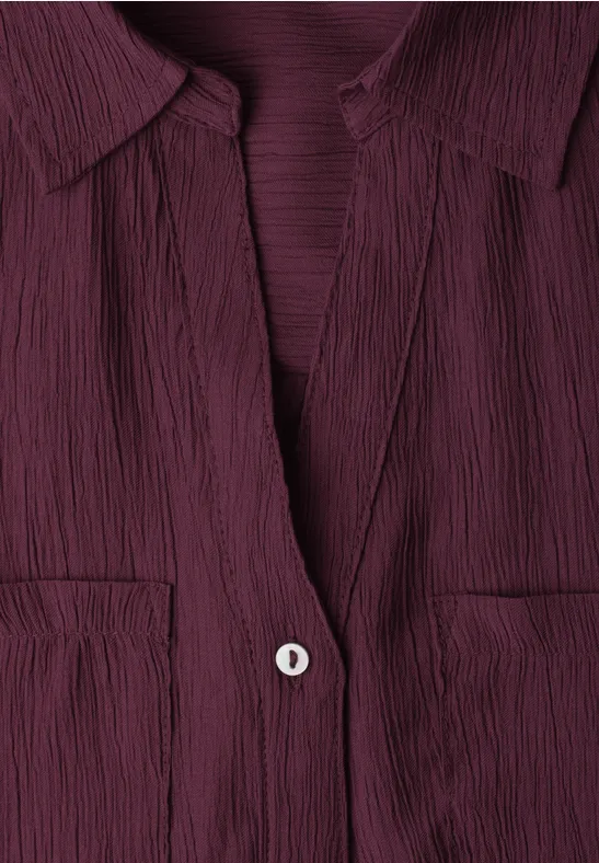 Close-up van een bordeauxroze, gestructureerd bloesje met kraag, V-hals, knoop en borstzakjes.