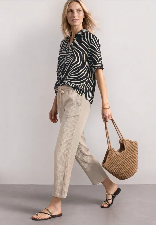 Personne en chemise zèbre noir et blanc, pantalon beige, sandales noires et sac en paille.
