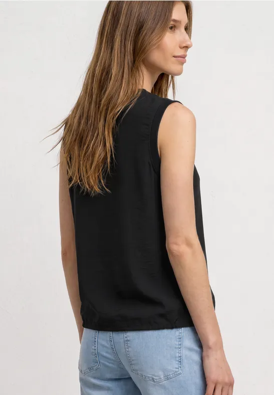 Rückenansicht einer Frau mit schwarzem Top ohne Ärmel und hellblauen Jeans.