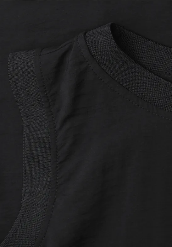 Schwarzes ärmelloses T-Shirt, Detailansicht von Rundhalsausschnitt und Ärmelausschnitt.