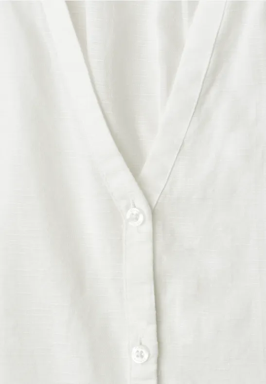 Close-up van een wit V-hals kledingstuk met knopen