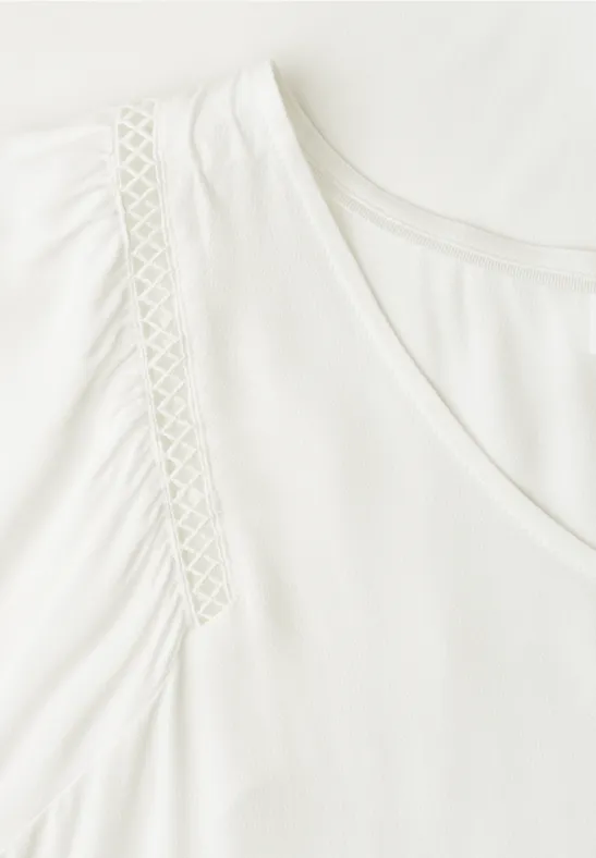 Weißes V-Ausschnitt-Shirt mit dekorativen Spitzen-Einsätzen an den Schultern.