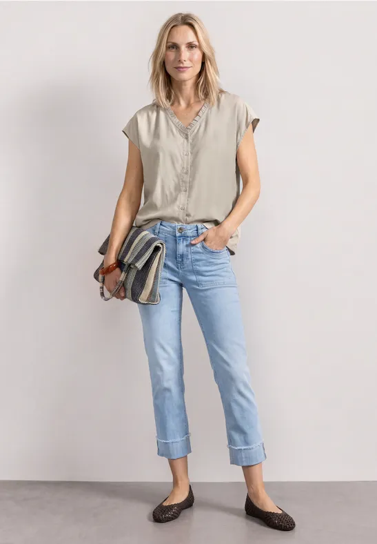 Vrouw met beige top, opgerolde spijkerbroek, bruine ballerina’s en gestreepte schoudertas.