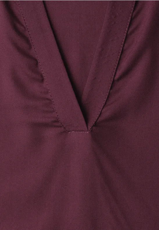 Nahaufnahme eines weinroten Kleidungsstücks mit tiefem V-Ausschnitt und sichtbarer Naht