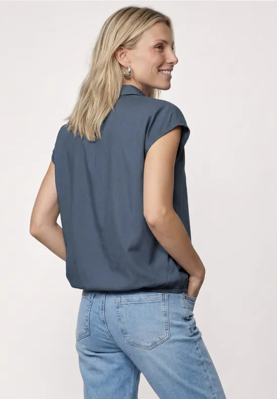 Rugaanzicht van een vrouw in blauw shirt en lichte spijkerbroek voor een lichte achtergrond.