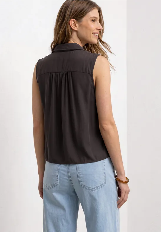 Frau von hinten in ärmellosem schwarzem Top und hellen Jeans, vor hellem Hintergrund.