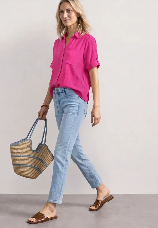 Vrouw in roze blouse en lichtblauwe jeans met strooien tas en bruine sandalen.