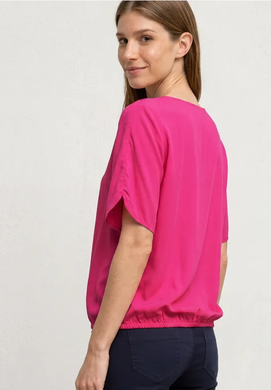 Een persoon van achteren met een roze top met korte mouwen en een donkere spijkerbroek.