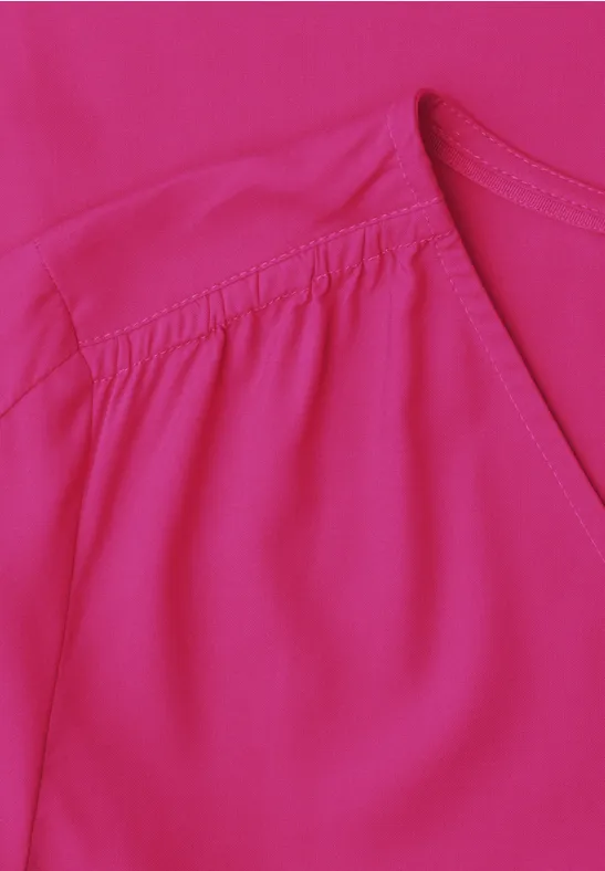 Close-up van de felroze blouse met subtiele plooien bij de schouder.
