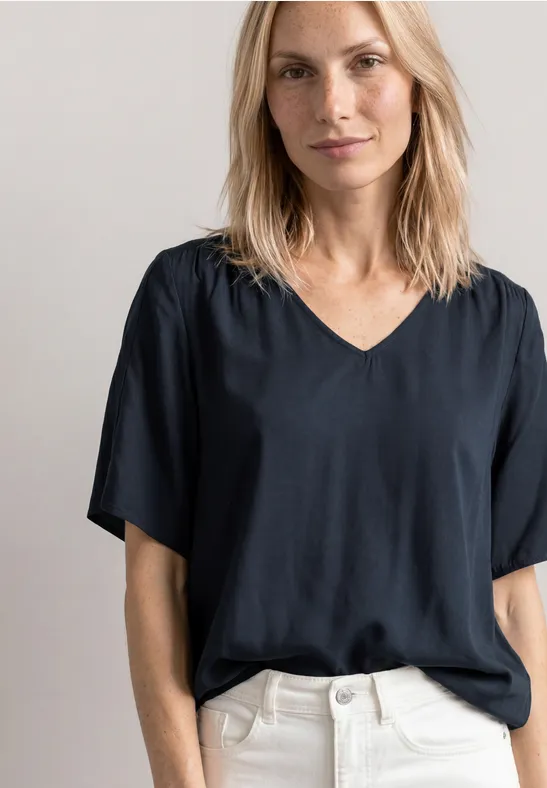 Vrouw in zwart V-halsshirt en witte broek, torso zichtbaar.