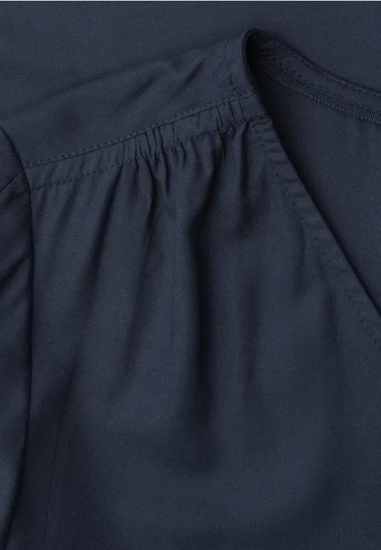 Close-up van een donkerblauw kledingstuk met plooien bij de schouder.