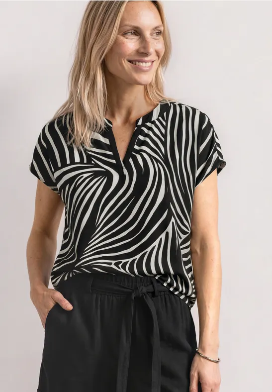 Een vrouw draagt een zwart-wit zebra-top en zwarte broek voor een witte achtergrond.