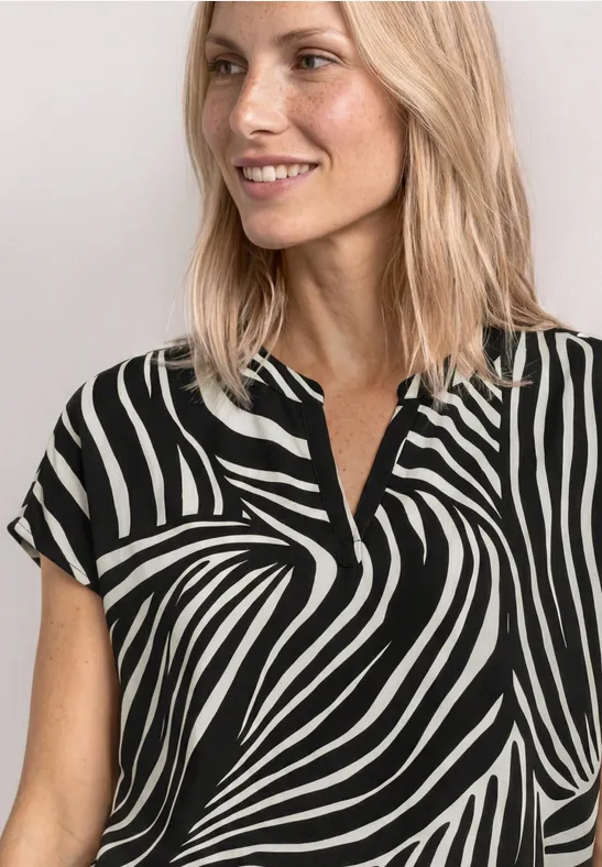 Een glimlachende vrouw met blond haar draagt een kort mouw blouse in zwart-witte zebraprint.