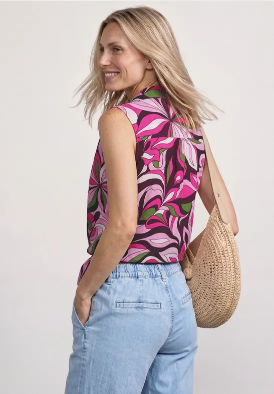 Vrouw van achteren met roze top met print, lichtblauwe jeans en een strooien tas.