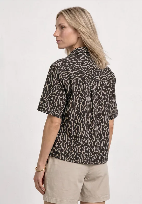 Vrouw van achteren in een korte blouse met luipaardprint en beige korte broek.