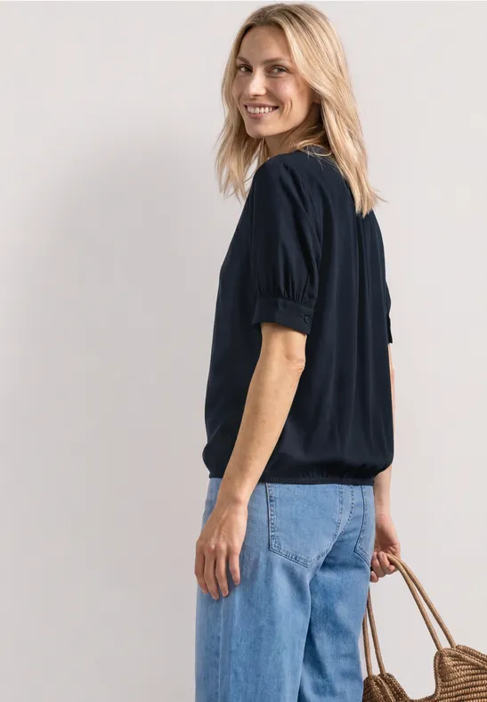Vrouw van opzij in zwarte blouse, blauwe jeans en een rieten tas.