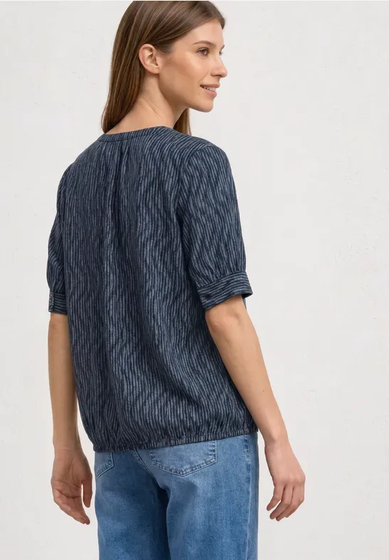 Vrouw van achteren in een donkerblauwe kabeltrui met driekwartmouwen en een lichtblauwe spijkerbroek.