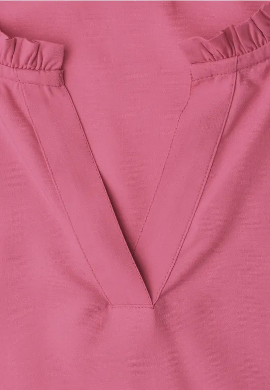 Nahaufnahme eines rosa Oberteils mit V-förmigem Ausschnitt und Rüschen an den Schultern.