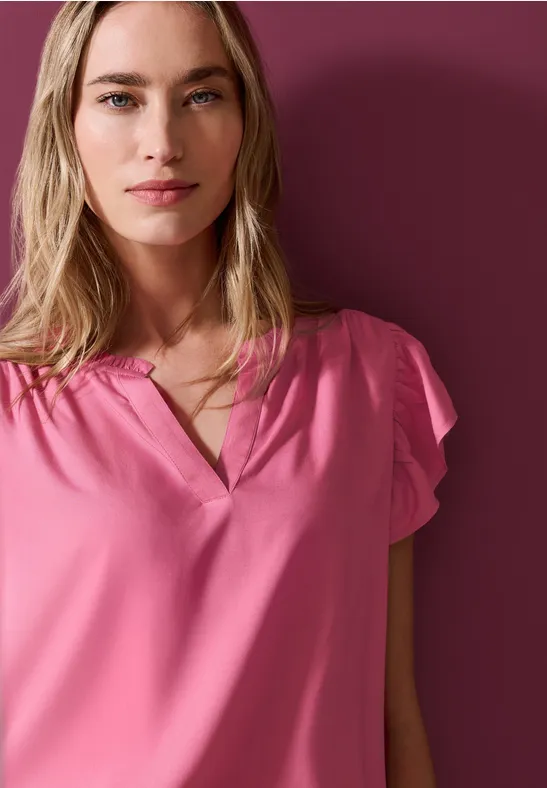 Eine blonde Frau in rosa Bluse vor dunklem rosafarbenen Hintergrund.