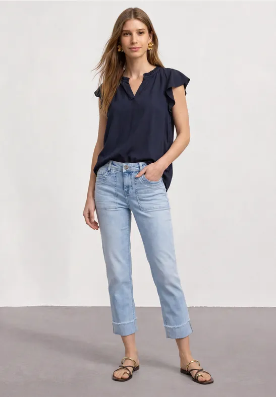 Eine Frau trägt eine dunkelblaue Bluse, helle umgeschlagene Jeans und schwarze Riemchensandalen.