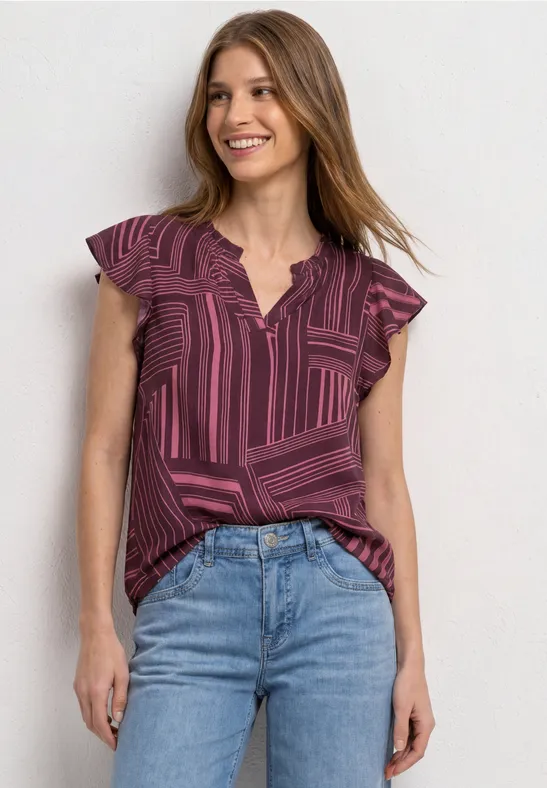 Lachende vrouw in paarse blouse met motief en korte volantmouwen, lichte spijkerbroek, voor een witte achtergrond.